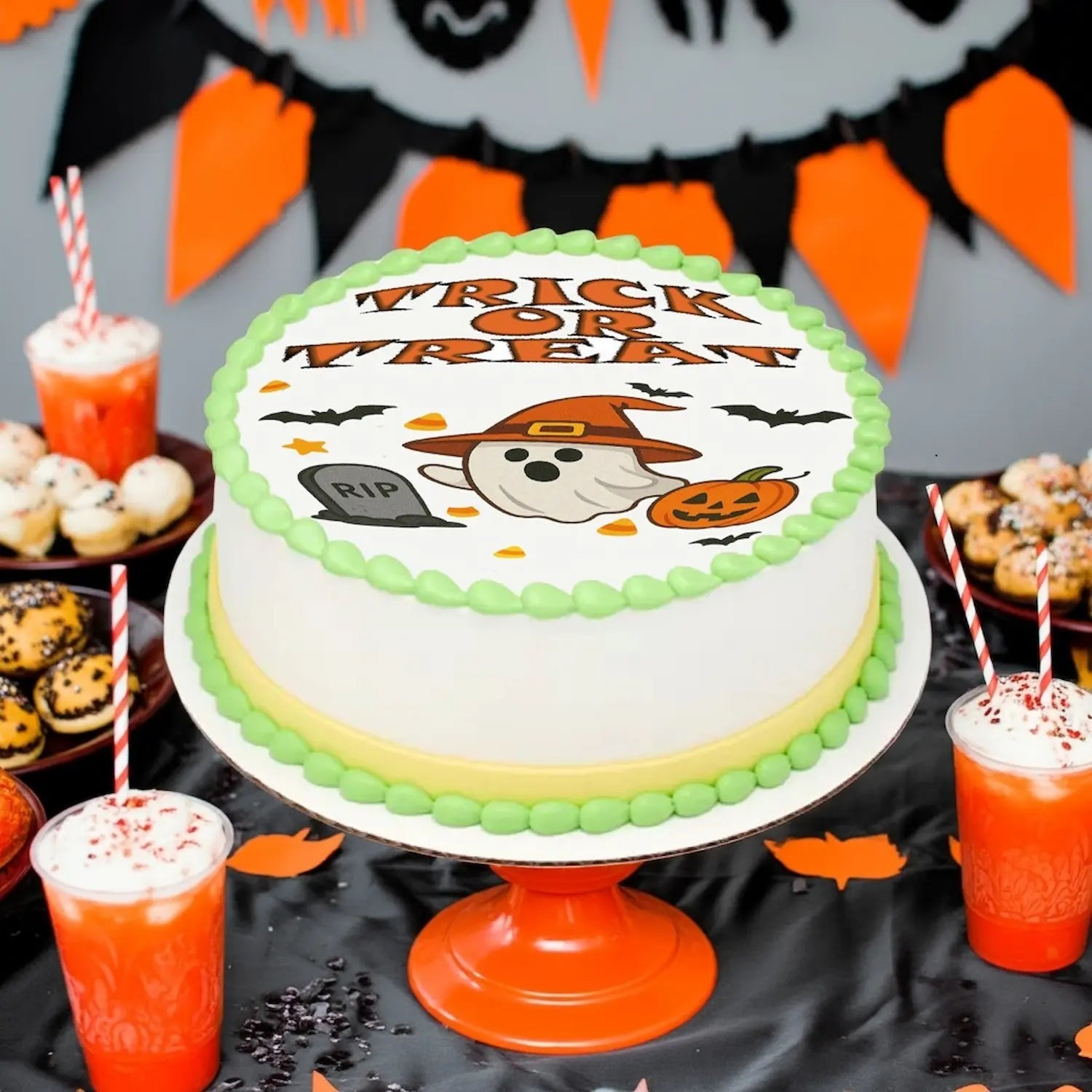 Halloween-themed edible image cake  topperon a pedistal on a table with cookies and drinks.