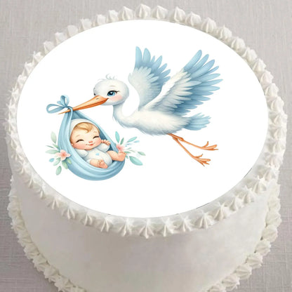 Precut 8-inch round edible icing topper featuring blue stork carrying a baby boy displayed on a frosted cake