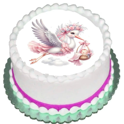 Precut 8-inch round edible icing topper featuring floral stork carrying a baby girl in a pink bundle on a cake with pink frosting trim