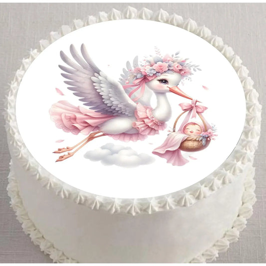 Precut 8-inch round edible icing topper featuring floral stork carrying a baby girl in a pink bundle displayed on a frosted cake